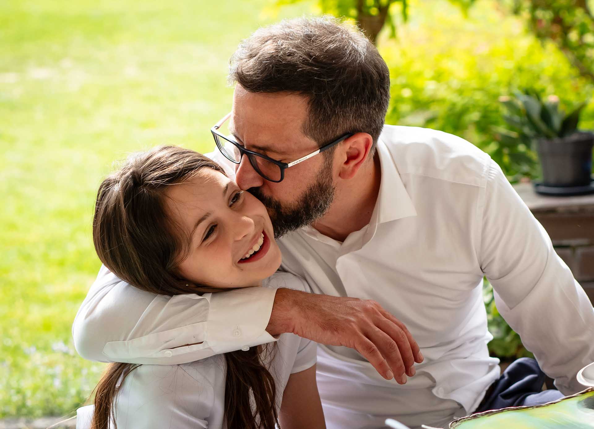 Komunia Święta Poli Tata obejmuje i całuje córkę w białej sukience i z wiankiem na głowie